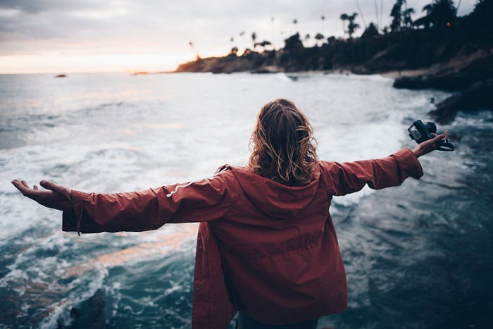 With outstretched arms, a woman overlooks a rugged coastline